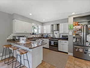 Kitchen with stainless steel appliances, white cabinets, a breakfast bar area, dark stone counters, and a peninsula