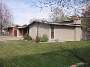 View of property exterior with a chimney, driveway, board and batten siding, a carport, and brick siding