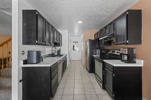 Kitchen with dark cabinetry, stainless steel appliances, light countertops, a textured ceiling, and light tile patterned flooring