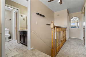 Stairs with carpet, a textured ceiling, and ceiling fan
