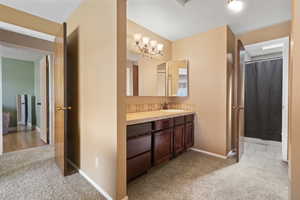 Master bedroom leading into bathroom with light carpet, vanity, curtained shower, and a textured ceiling