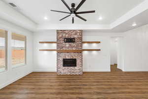 Unfurnished living room with dark wood-type flooring, ceiling fan, a fireplace, a tray ceiling, and recessed lighting