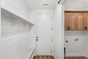 Laundry room with a barn door, electric dryer hookup, wood finished floors, washer hookup, and cabinet space