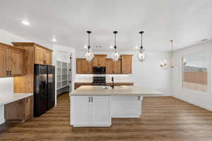 Dual tone kitchen with dark wood-type flooring, black fridge with ice dispenser, two tone color scheme, an island with sink, and gas range