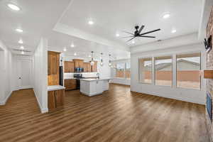 Kitchen with light countertops, wood finish cabinetry, ceiling fan, suspended lighting, and a kitchen island with sink