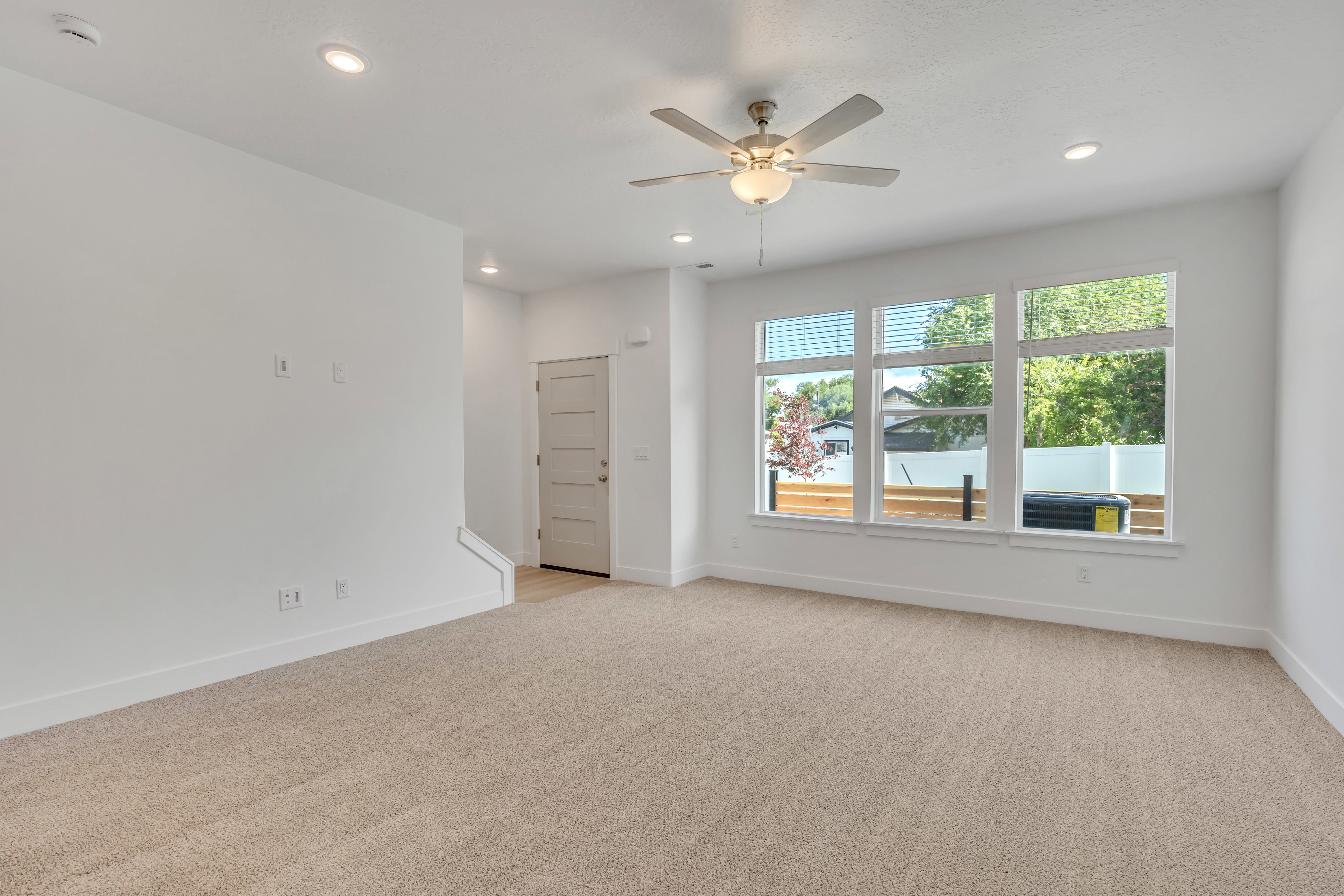 Spacious living area featuring light-toned carpeting, white walls, and recessed lighting