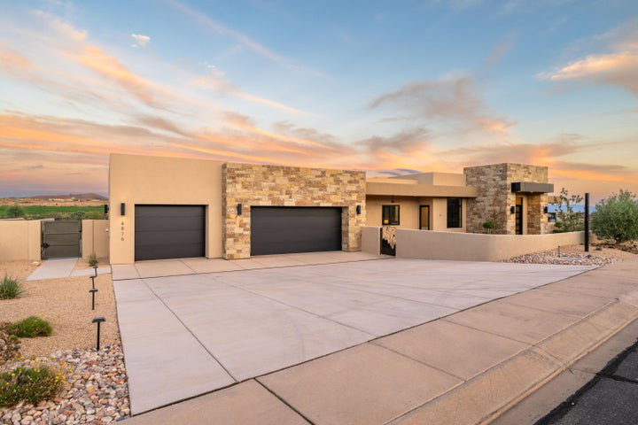 View of front facade featuring a gate, stone siding, an attached garage, concrete driveway, and stucco siding