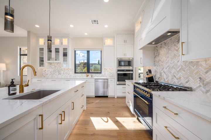 Kitchen with glass fronted cabinets, stainless steel appliances, white cabinets, light stone countertops, and light wood-style flooring