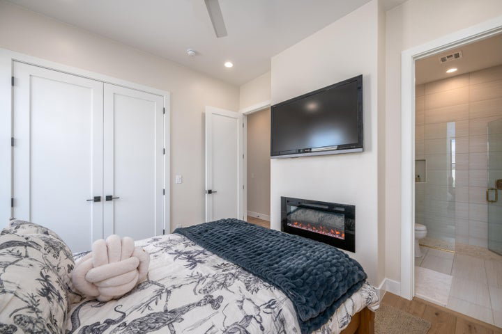Bedroom featuring a closet, light wood finished floors, a glass covered fireplace, a ceiling fan, and recessed lighting