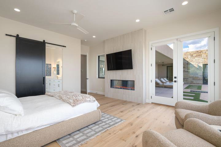 Bedroom featuring a barn door, light wood finished floors, access to exterior, a ceiling fan, and ensuite bathroom