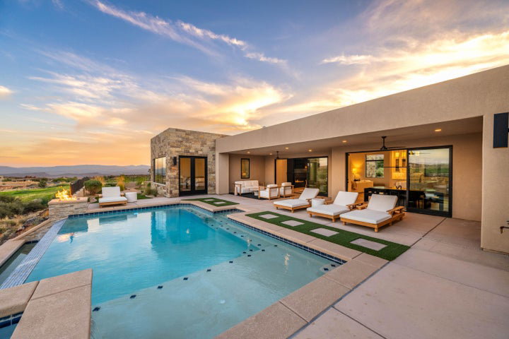 Back of property at dusk featuring stone siding, a patio area, an outdoor pool, and stucco siding