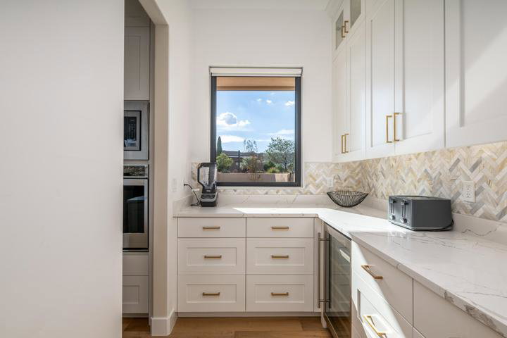 Kitchen featuring white cabinets, stainless steel appliances, wine cooler, light stone counters, and light wood-type flooring