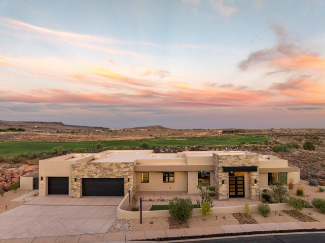 Pueblo revival-style home featuring stone siding, a garage, stucco siding, and concrete driveway