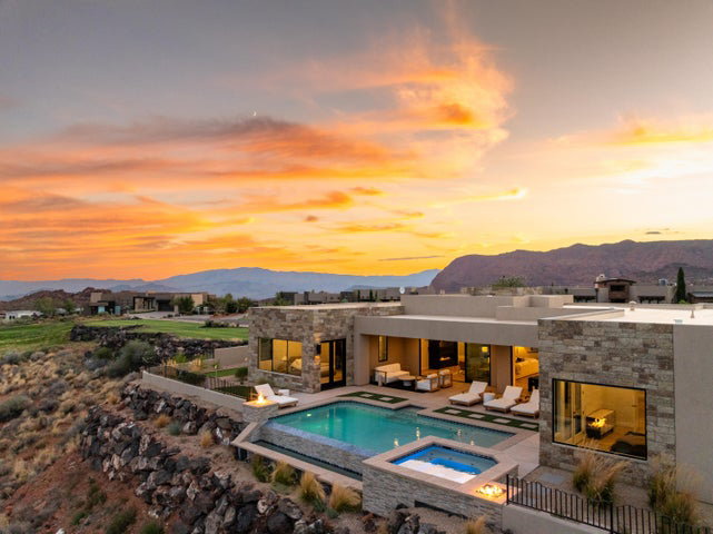 Back of property at dusk featuring a patio area, stone siding, a mountain view, and an outdoor stone fireplace