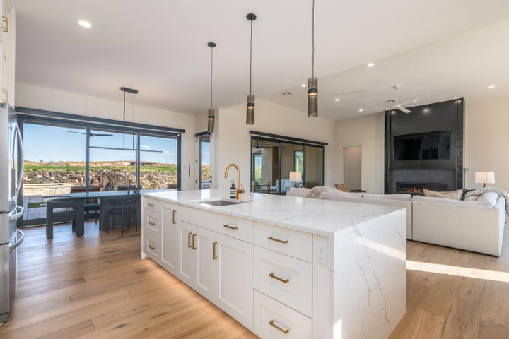 Kitchen featuring white cabinetry, open floor plan, an island with sink, light stone counters, and decorative light fixtures