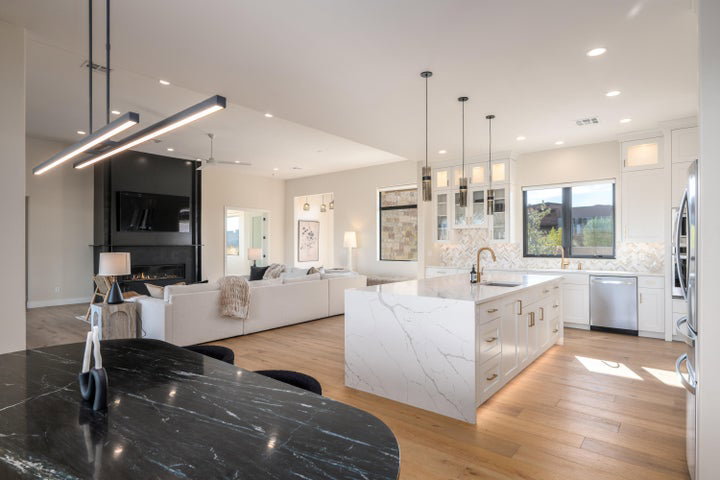 Kitchen with white cabinets, glass fronted cabinets, light stone countertops, an island with sink, and light wood-style flooring