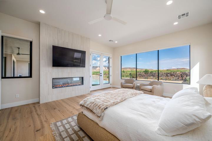 Bedroom with a fireplace, access to outside, light wood-type flooring, ceiling fan, and french doors