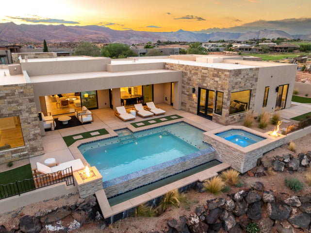 Back of house at dusk with an in-ground hot tub, an outdoor pool, a patio, and a mountain view