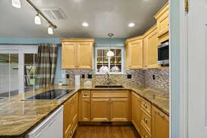 Kitchen featuring light wood finish cabinetry, dark stone counters, dishwasher, dark wood-style flooring, and black electric stovetop