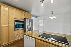 Kitchen with stainless steel appliances, light wood finish cabinetry, dark wood-type flooring, suspended lighting, and dark stone counters