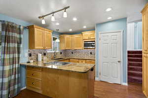 Kitchen featuring a peninsula, backsplash, dark wood-type flooring, light wood finish cabinetry, and vaulted ceiling