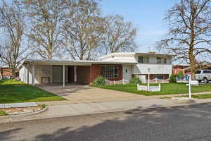 View of front of property featuring a front lawn, brick siding, an attached carport, concrete driveway, and a chimney