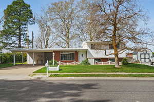 View of front of home featuring an attached carport, brick siding, driveway, and a storage shed