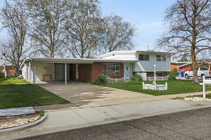 View of front facade featuring a front lawn, brick siding, a carport, and driveway
