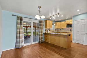 Kitchen featuring light stone countertops, a peninsula, a chandelier, backsplash, and light wood-type flooring