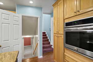 Kitchen featuring stainless steel oven, light wood finish cabinets, and dark wood-style flooring