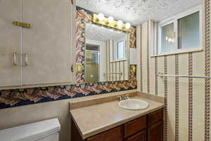 Full bathroom featuring wallpapered walls, vanity, a textured ceiling, and a shower stall