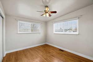 Empty room featuring lofted ceiling, wood-type flooring, a ceiling fan, and healthy amount of natural light