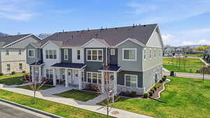 Townhome with a porch, a front lawn, stone siding, and a shingled roof