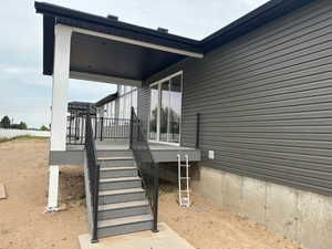 Rear exterior featuring a covered deck with white columns, dark gray composite decking, and black metal railings