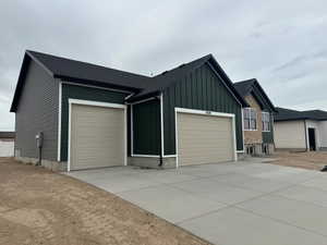 Contemporary exterior featuring dark green vertical siding, contrasting gray horizontal siding, an attached two-car garage with tan doors, a concrete driveway, and a stone facade accent