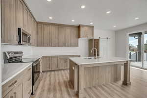 Kitchen featuring stainless steel appliances, a kitchen island with sink, recessed lighting, light wood-style flooring, and a barn door