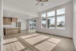 Unfurnished living room featuring recessed lighting, a barn door, ceiling fan, light wood-type flooring, and a high ceiling