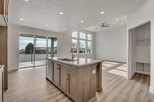 Kitchen with a kitchen island with sink, light wood-style floors, plenty of natural light, light stone counters, and a textured ceiling