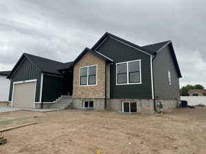 Contemporary exterior featuring dark green siding, stone accents, black-trimmed windows, a light-colored garage door, and a concrete pathway