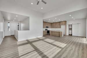 Unfurnished living room with a barn door, recessed lighting, a ceiling fan, and light wood-type flooring