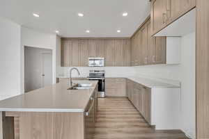 Kitchen with recessed lighting, stainless steel appliances, an island with sink, light wood-style flooring, and light stone countertops