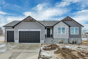 View of front facade featuring a garage, stone siding, driveway, and roof with shingles
