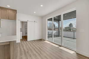 Unfurnished dining area featuring a barn door, light wood-style floors, and recessed lighting