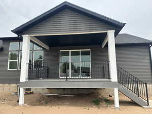 Covered patio featuring a sliding glass door, black metal railing, composite decking, and exterior stairs