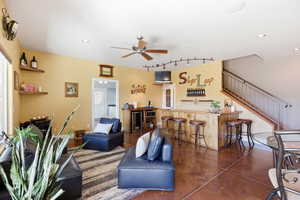 Living room with finished concrete flooring, a ceiling fan, a bar, beverage cooler, and rail lighting