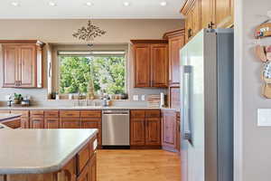 Kitchen featuring freestanding refrigerator, wood finish cabinetry, stainless steel dishwasher, light wood-style floors, and recessed lighting