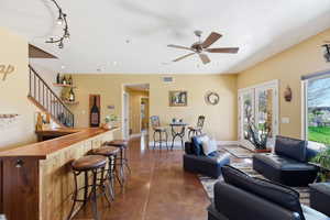 Living room with finished concrete floors, a ceiling fan, a dry bar, and rail lighting