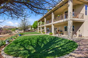 Rear view of property with stucco siding, a balcony, a yard, a patio area, and a mountain view
