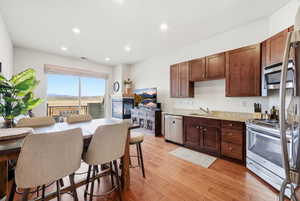 Kitchen with stainless steel appliances, light stone countertops, light wood-style floors, dark wood finish cabinetry, and recessed lighting