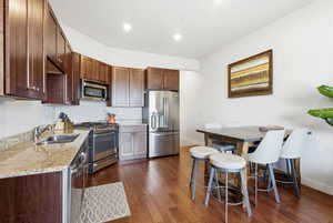 Kitchen with stainless steel appliances, light stone counters, dark wood finish cabinets, and dark wood-style flooring